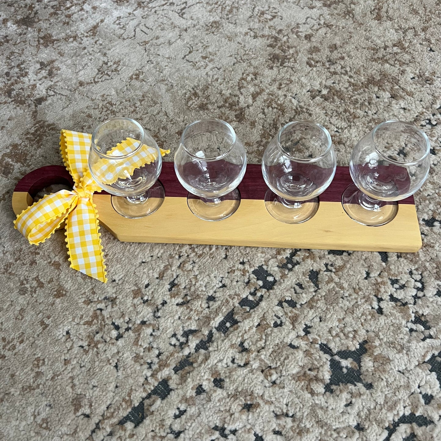 Handcrafted bourbon flight board made from purpleheart and yellowheart wood, featuring four tasting glasses arranged on a vibrant wood grain surface.