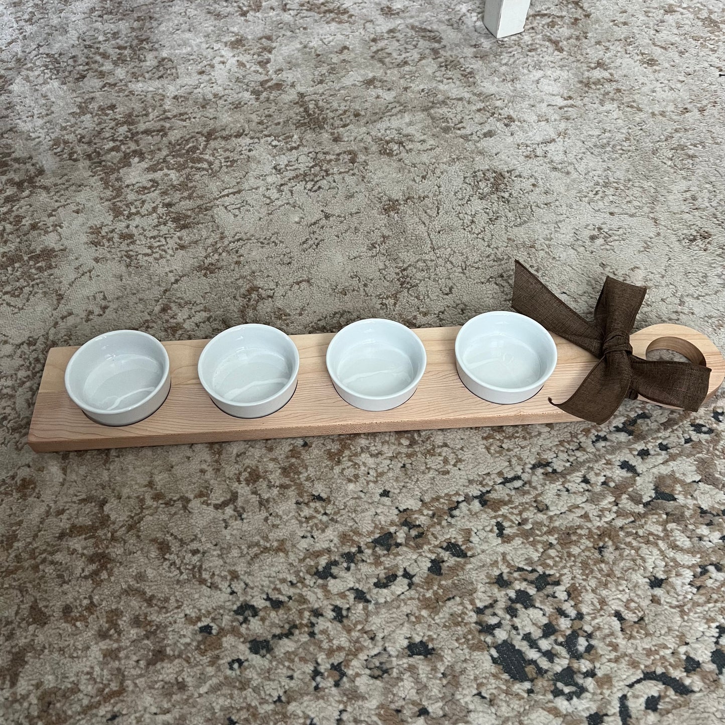 Handcrafted cherry and maple wood flight with a rounded handle, bow accent, and four white dipping bowls. Approximately 24 inches long.