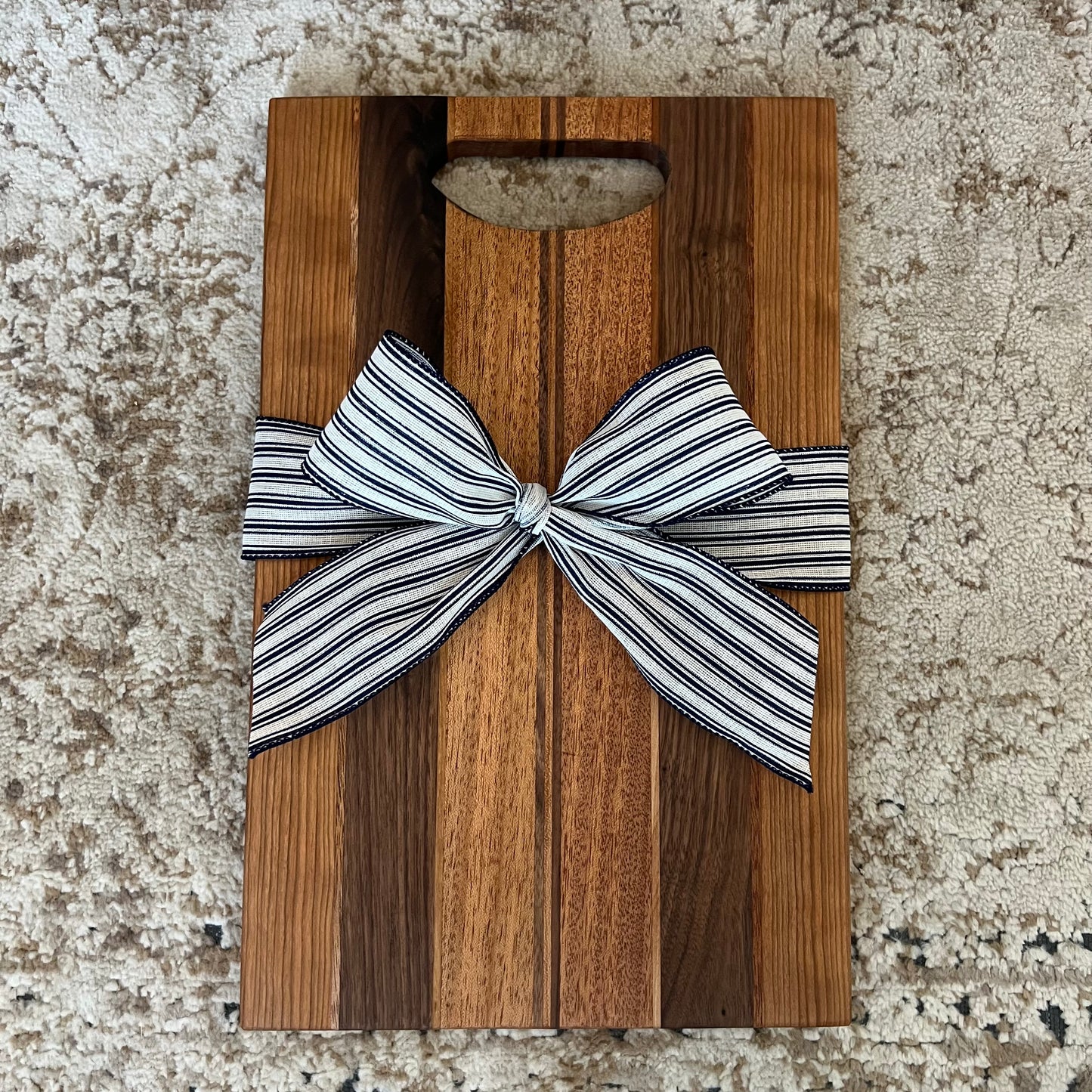 Handmade charcuterie board with handle, crafted from mahogany, cherry, and walnut, tied with a black and white striped bow