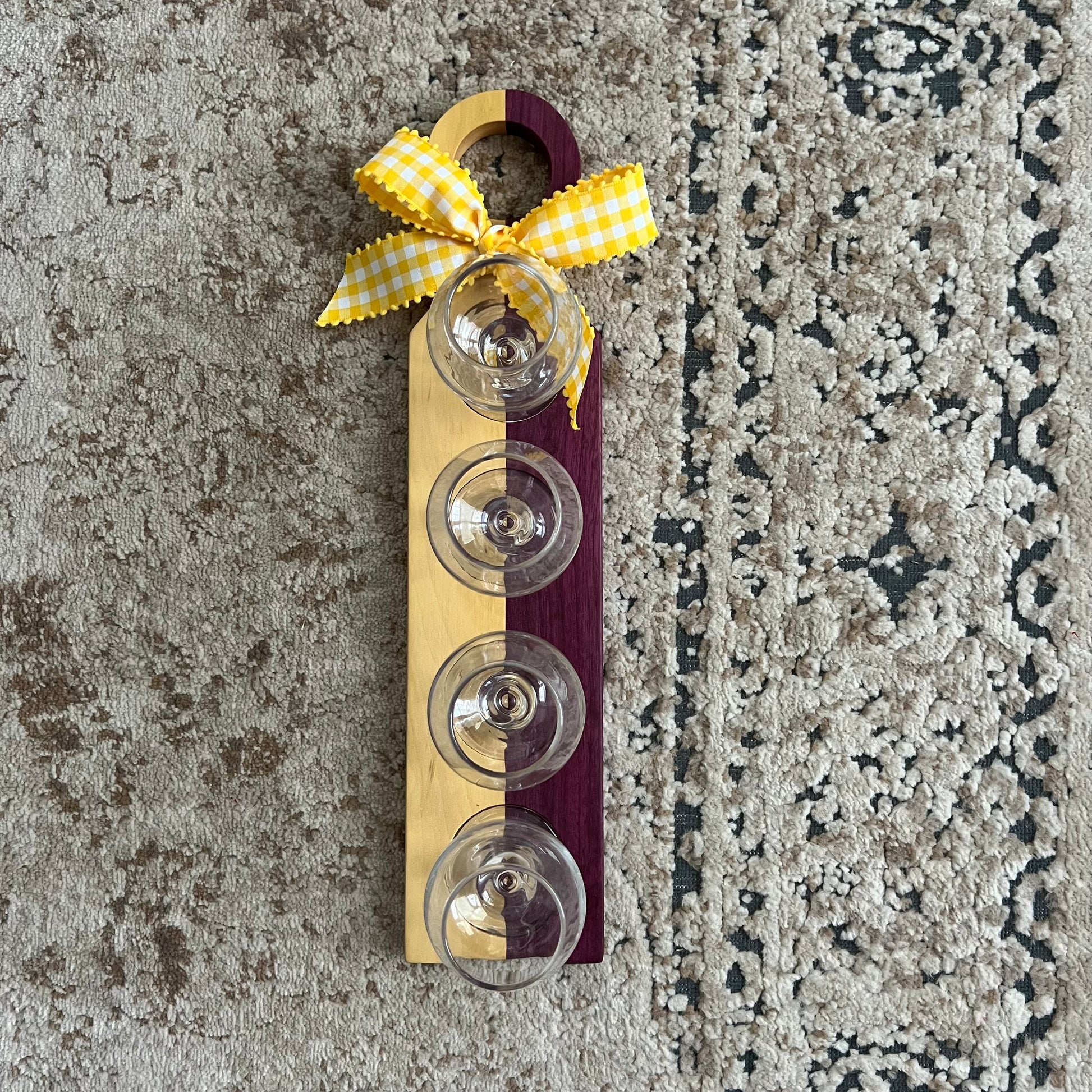 Handcrafted bourbon flight board made from purpleheart and yellowheart wood, featuring four tasting glasses arranged on a vibrant wood grain surface.