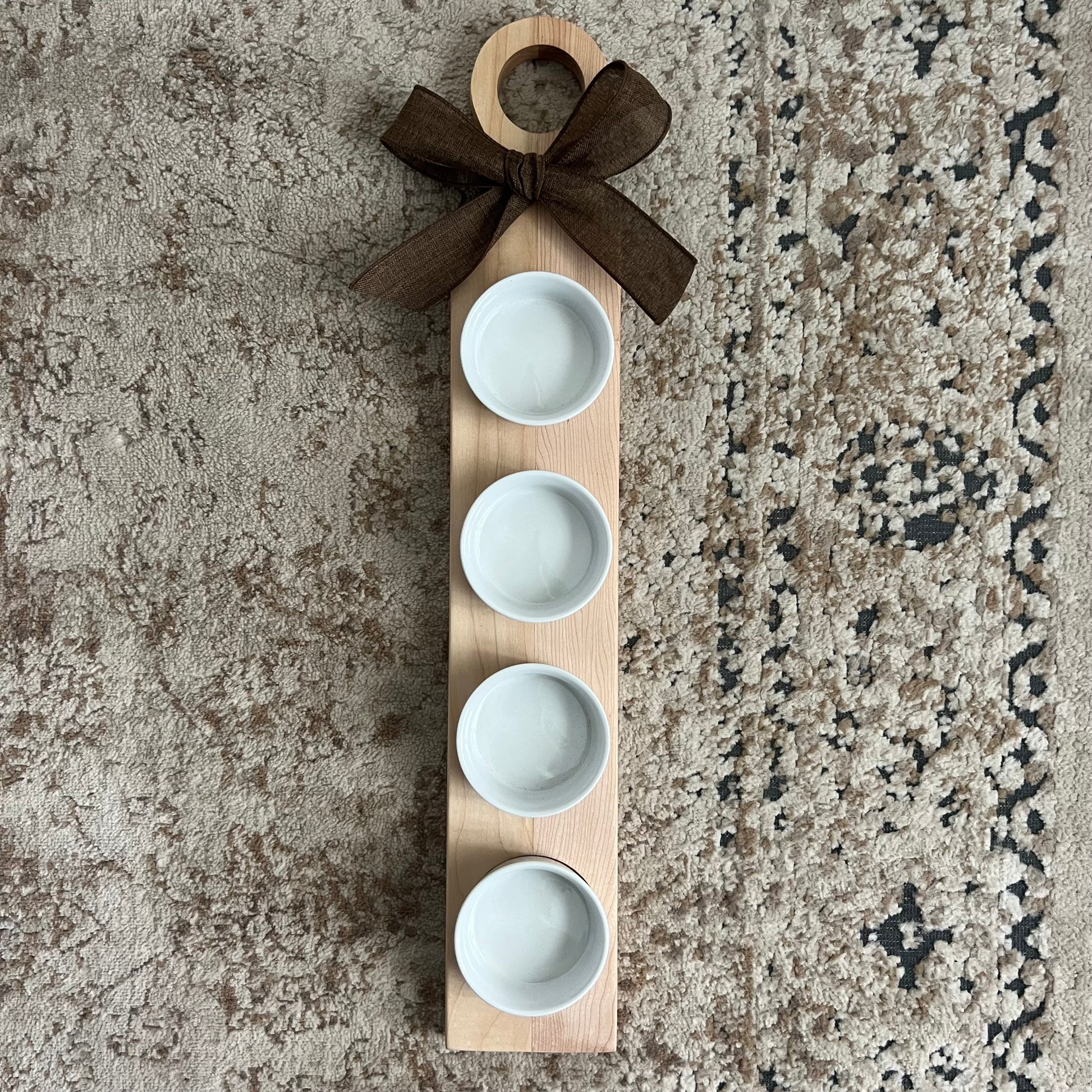 Handcrafted cherry and maple wood flight with a rounded handle, bow accent, and four white dipping bowls. Approximately 24 inches long.