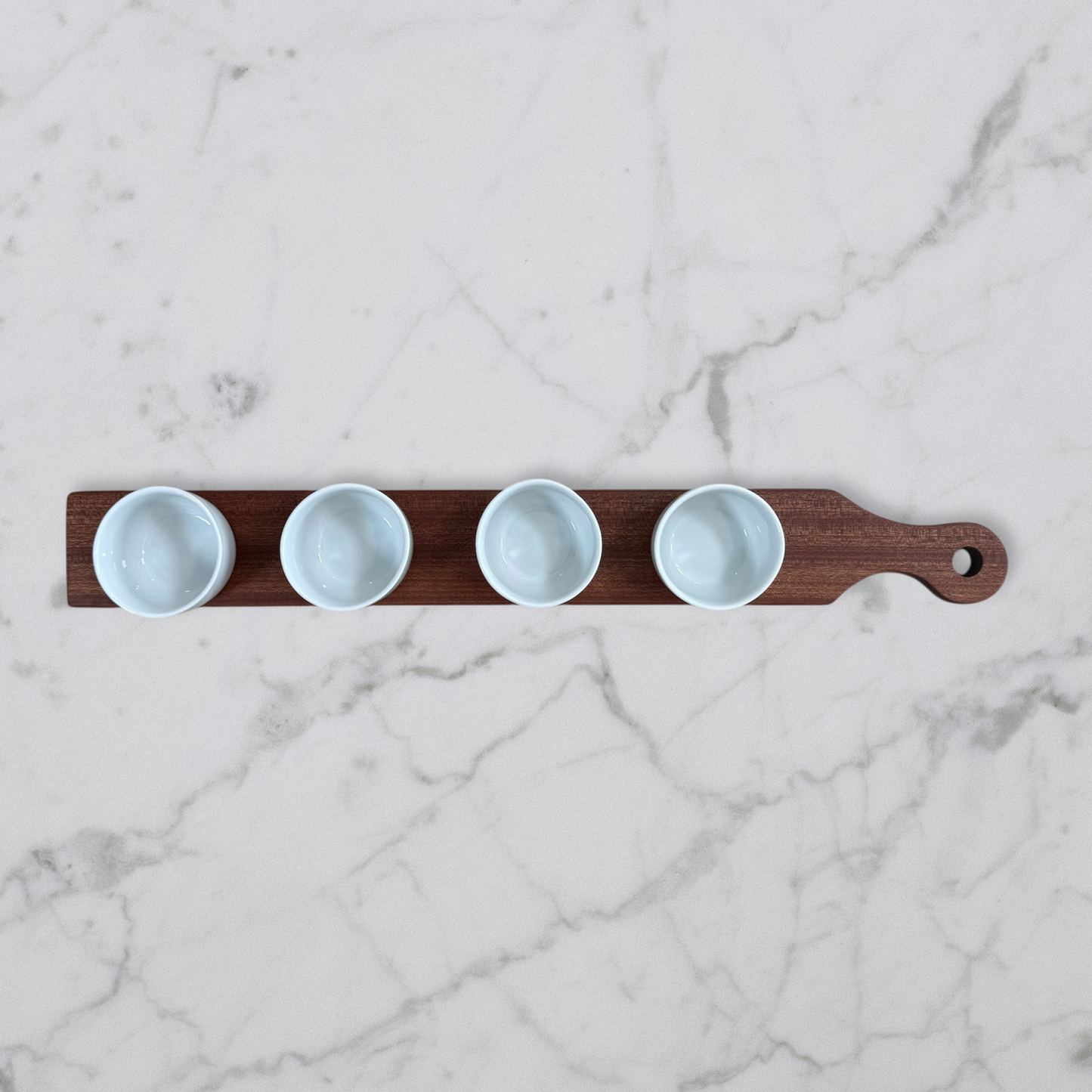 Cherry and maple dip flight board with handle and four white dipping bowls on marble surface