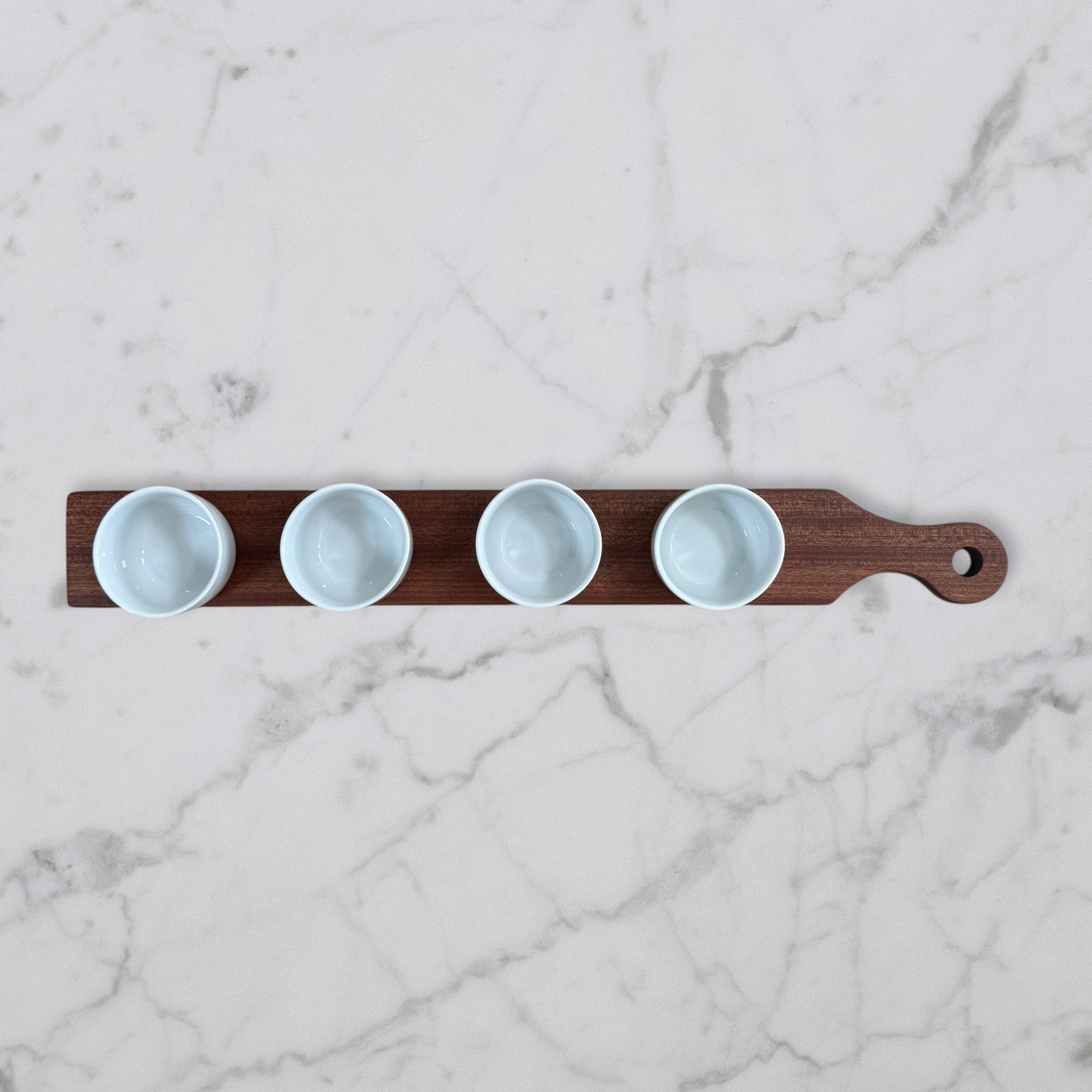 Cherry and maple dip flight board with handle and four white dipping bowls on marble surface