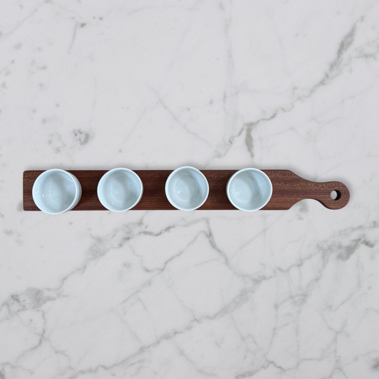 Cherry and maple dip flight board with handle and four white dipping bowls on marble surface