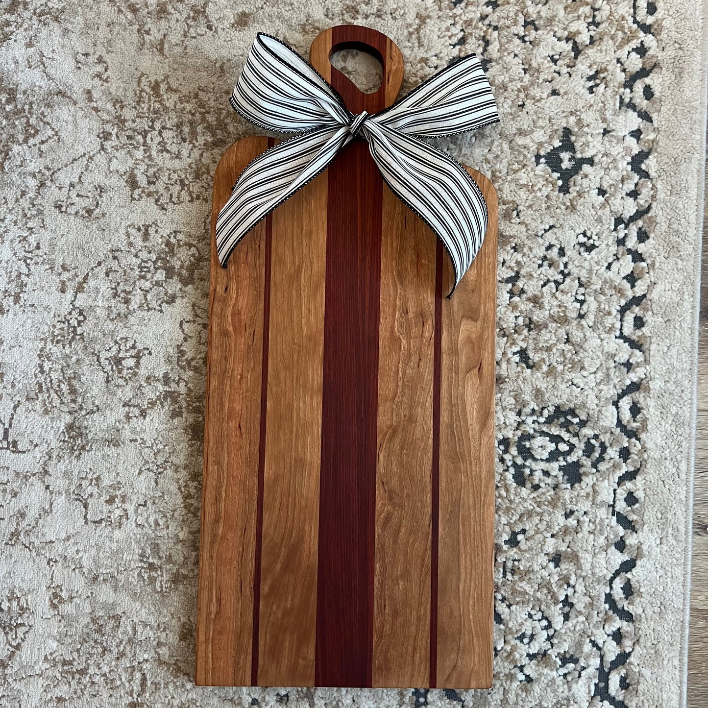 Handcrafted charcuterie board made from padauk and cherry wood with a bow on the handle