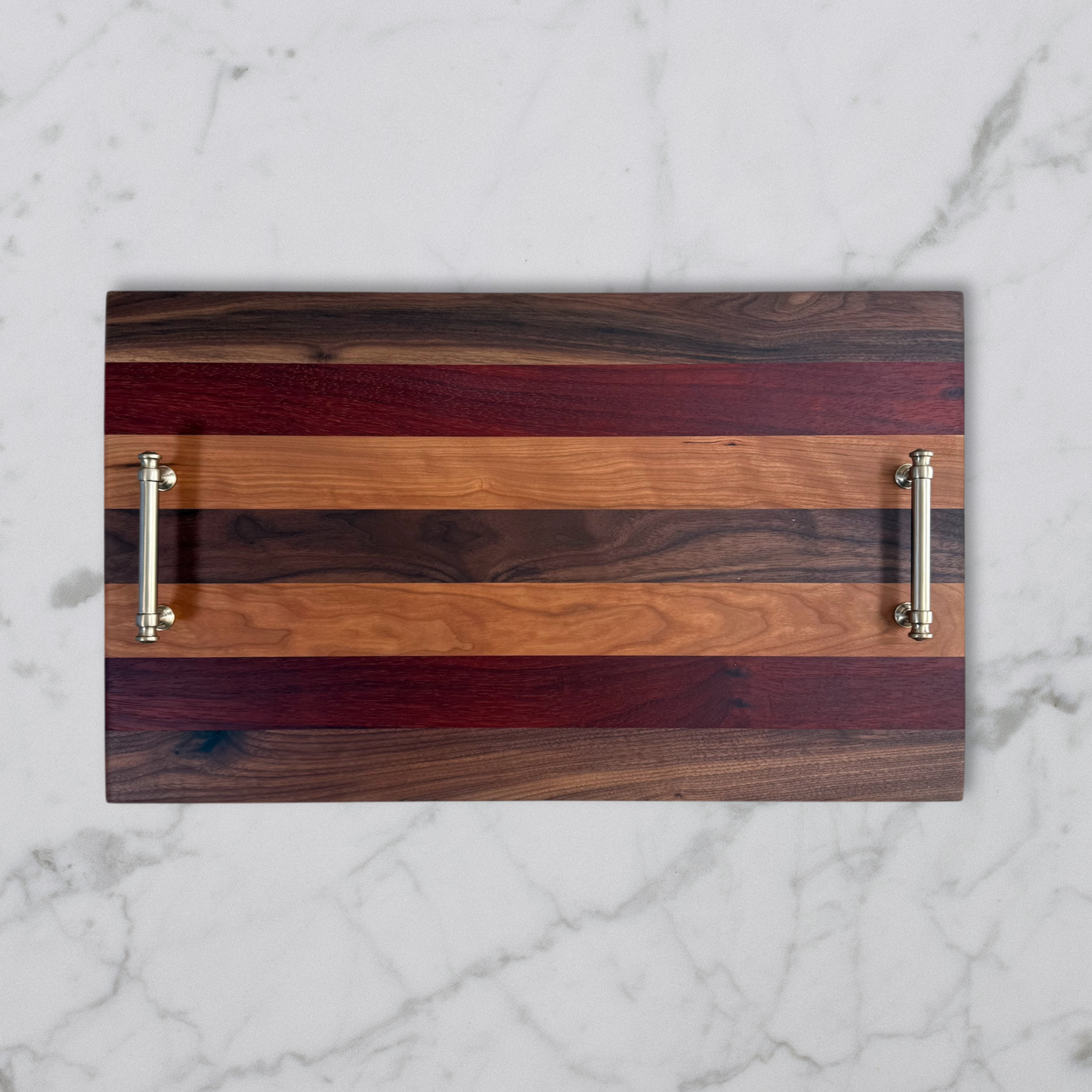 Wooden serving tray with striped pattern and metallic handles on a marble background