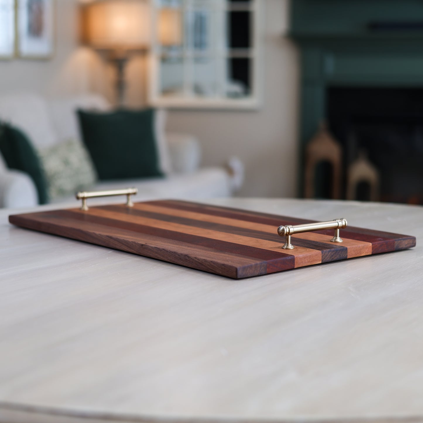 Wooden serving tray with striped pattern and metallic handles on a table in a blurred living room setting