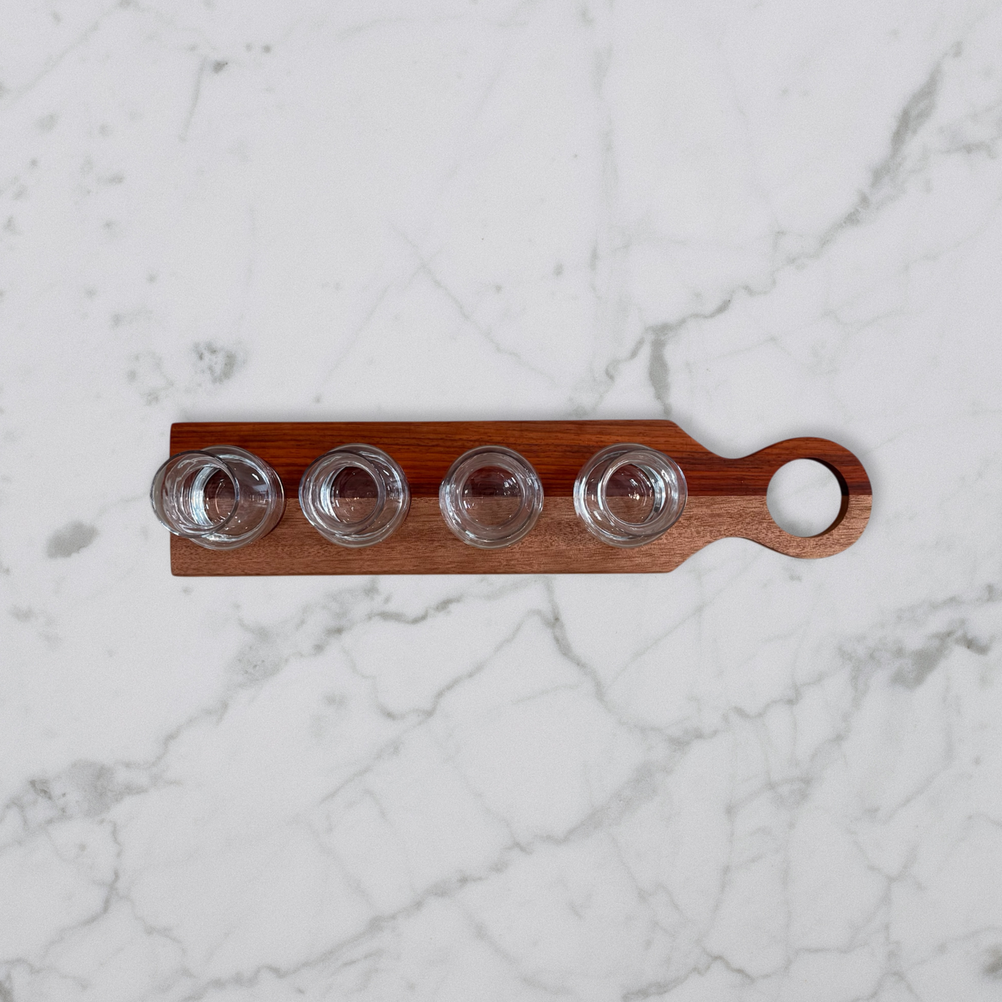 Handcrafted padauk and okoume wine flight board with four glass carafes on marble surface
