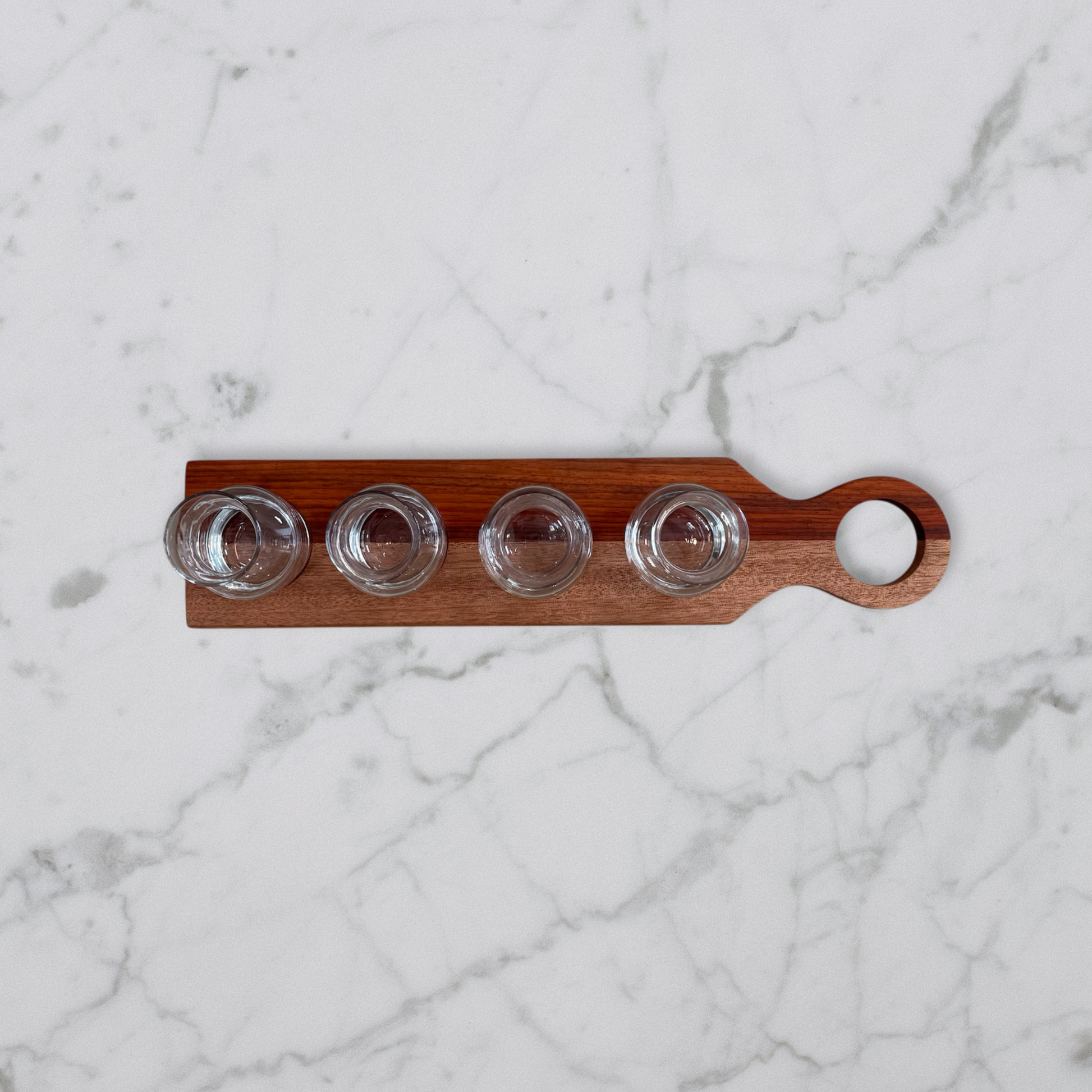 Handcrafted padauk and okoume wine flight board with four glass carafes on marble surface