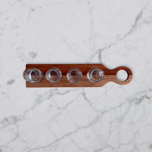 Handcrafted padauk and okoume wine flight board with four glass carafes on marble surface