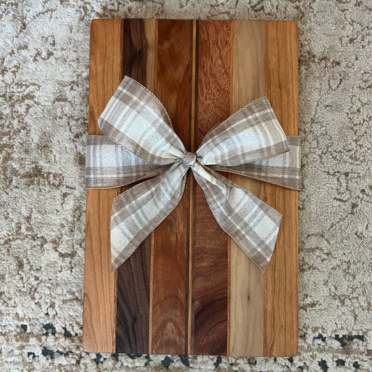 Handcrafted charcuterie board made from mahogany, cherry, and walnut with a plaid bow, displayed on a neutral rug