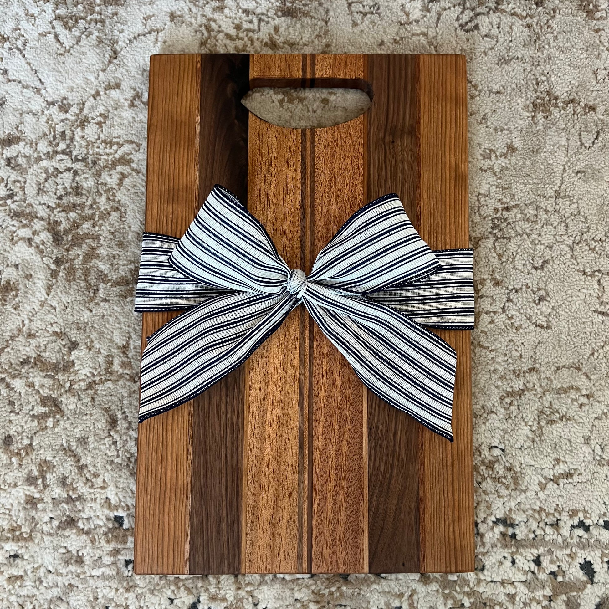 Handmade charcuterie board with handle, crafted from mahogany, cherry, and walnut, tied with a black and white striped bow