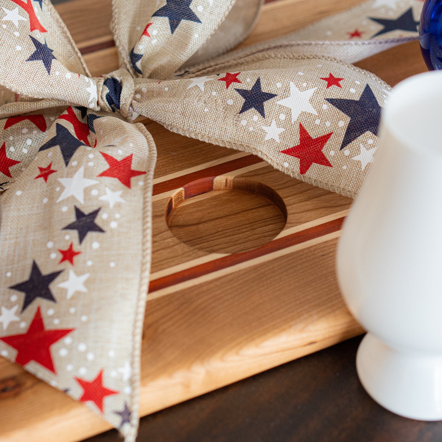 Patriotic wooden bourbon flight board with a decorative ribbon featuring red, white, and blue stars on a wooden surface.
