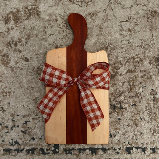 12.5" x 6" handcrafted charcuterie board made from maple and padauk wood with curved handle and gingham bow