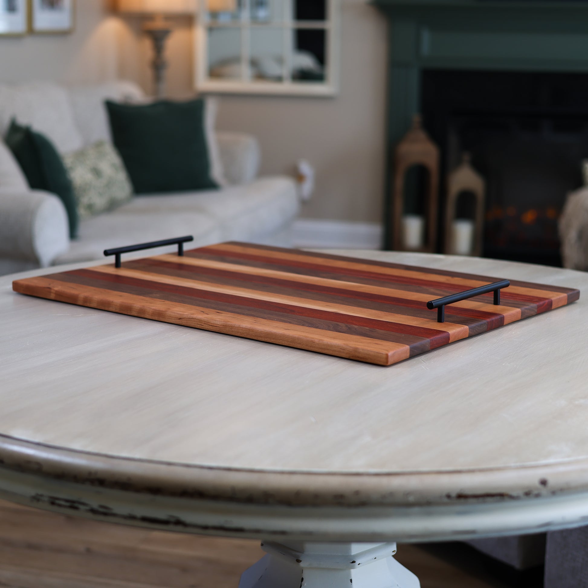 Wooden stove top tray with striped pattern and black handles on a round table in a living room setting
