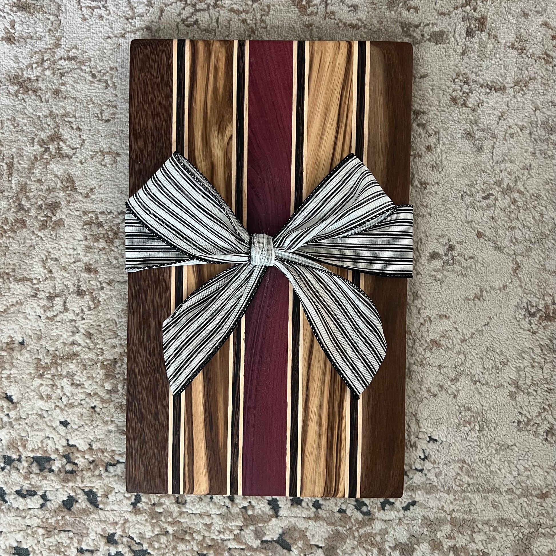 Handcrafted serving board with stripes of brownheart, purpleheart, maple, zebrawood, and wenge. Measures approx. 15¾ by 9¾ inches with a smooth finish.