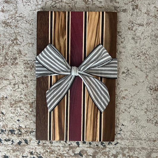 Handcrafted serving board with stripes of brownheart, purpleheart, maple, zebrawood, and wenge. Measures approx. 15¾ by 9¾ inches with a smooth finish.