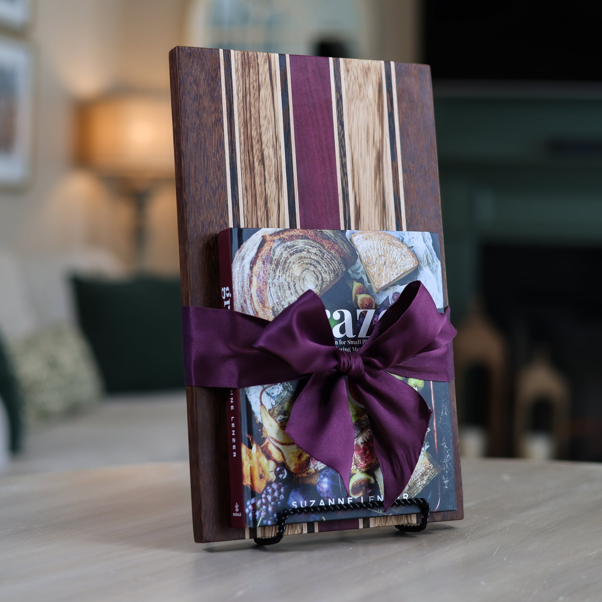 Handcrafted striped wood charcuterie board made from brownheart, purpleheart, maple, zebrawood, and wenge, paired with the Graze book and wrapped with ribbon on a living room table