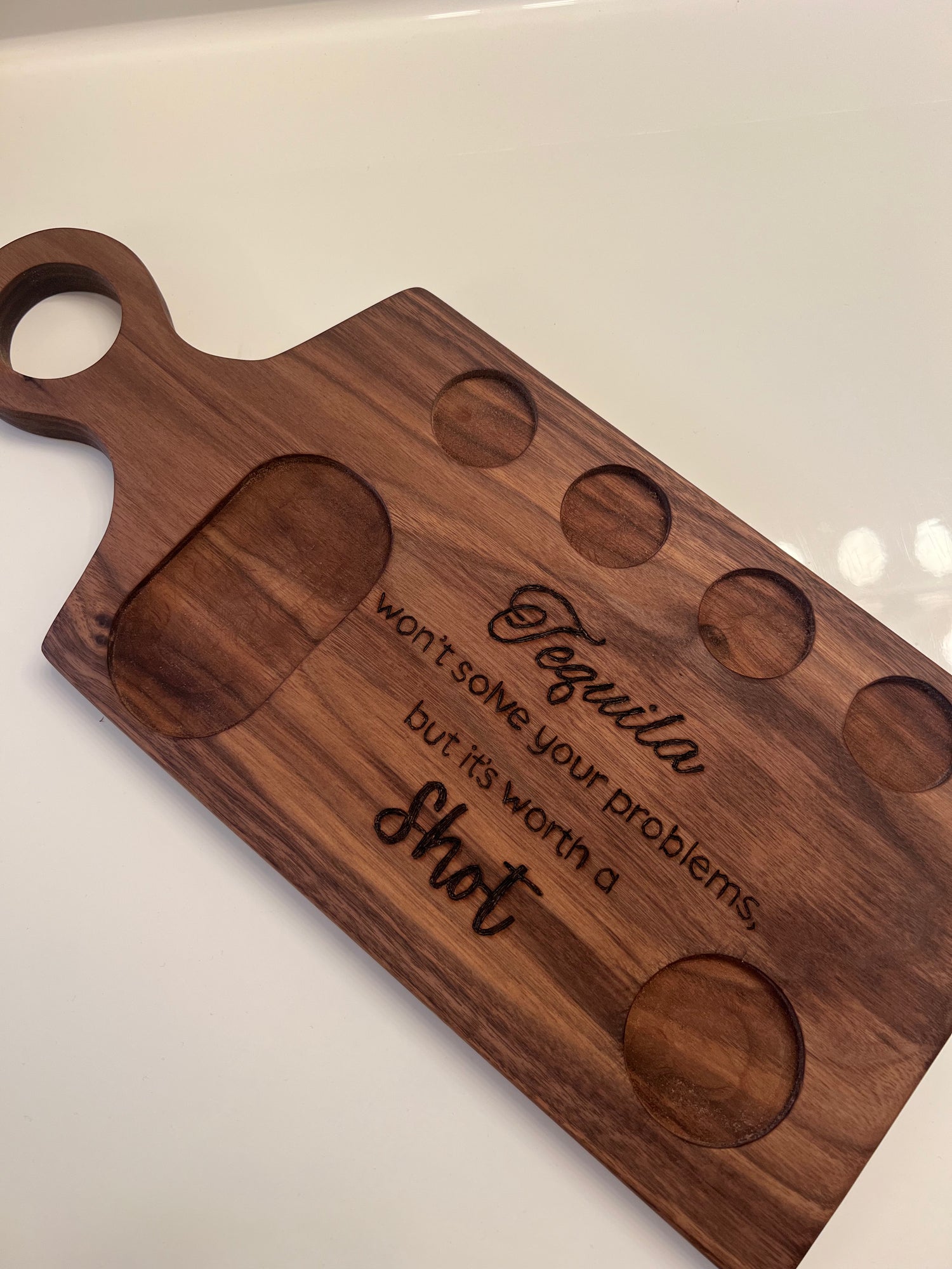 Handcrafted walnut tequila flight board with engraved quote: "Tequila won’t solve your problems, but it’s worth a shot," featuring cutouts for shot glasses.