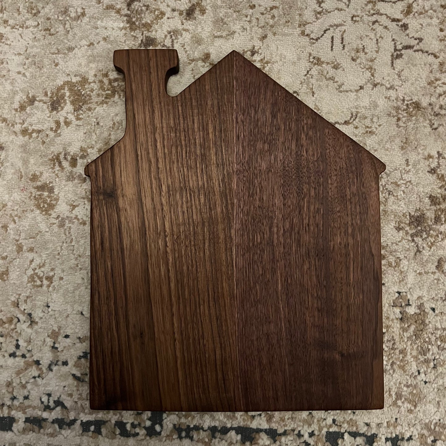 Handcrafted walnut charcuterie board in the shape of a house, featuring natural wood grain and peaked roof silhouette