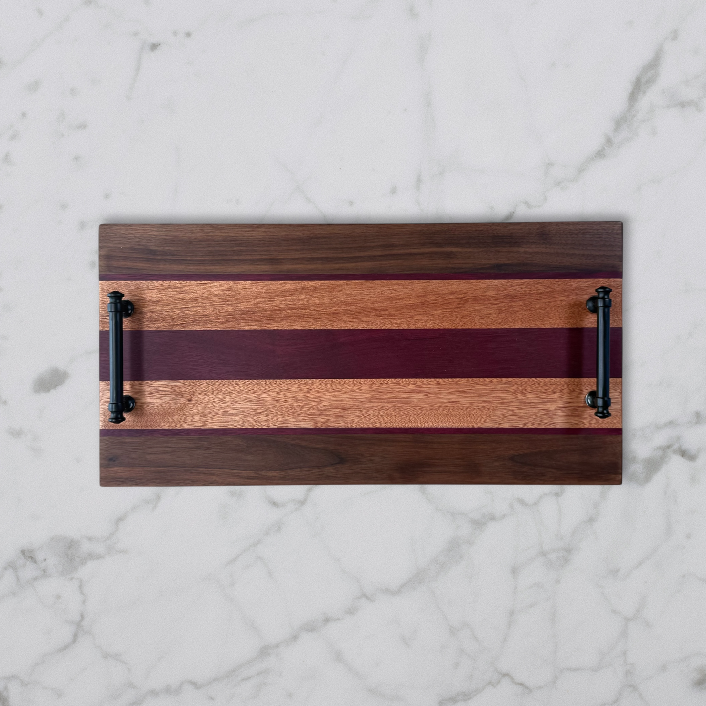 Wooden serving board with black handles on a marble surface