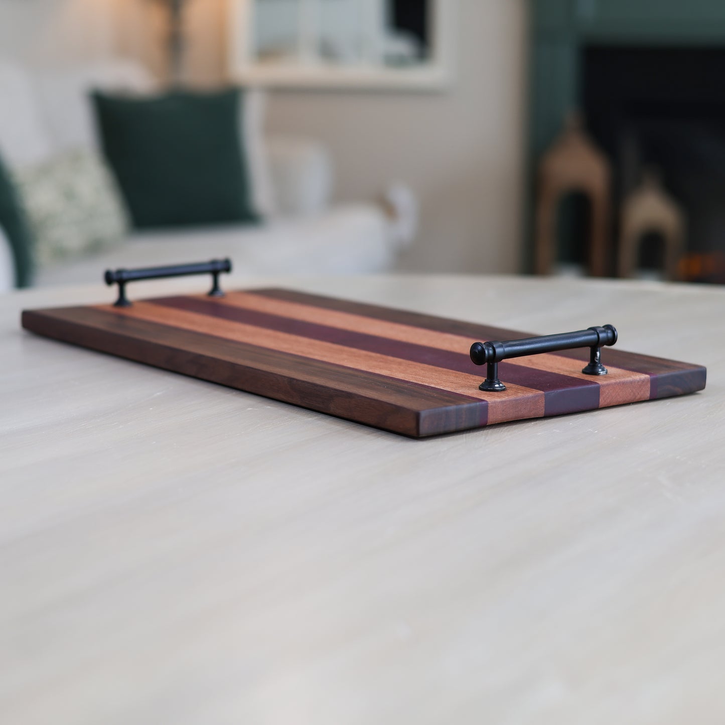 Wooden serving board with black handles on a light surface, blurred indoor background