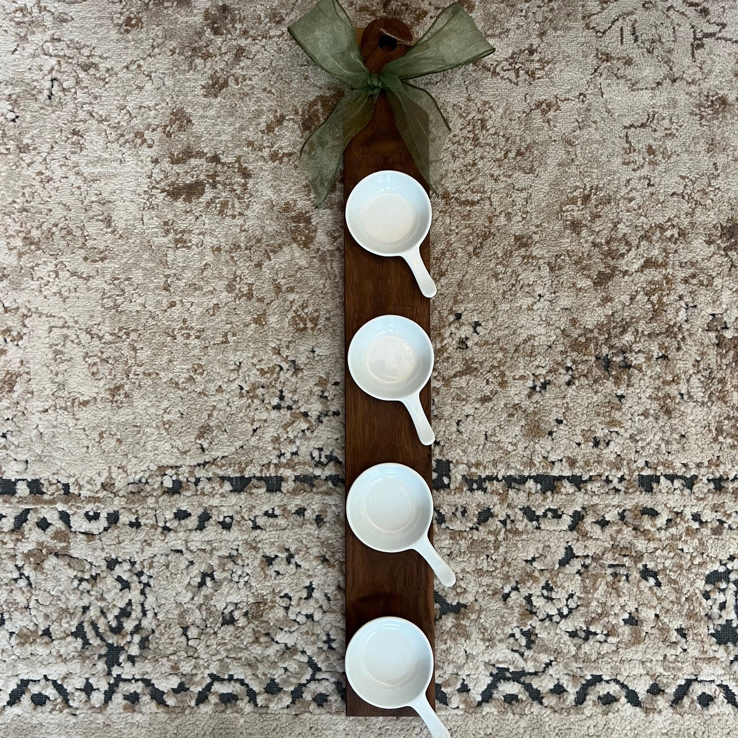 A handcrafted walnut wood flight board with 4 white handled mini bowls, accented with a green bow, ideal for dips, sauces, or tastings.
