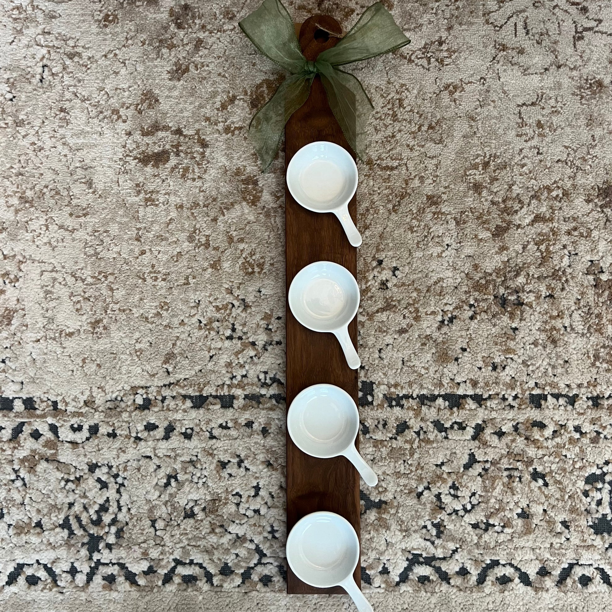 A handcrafted walnut wood flight board with 4 white handled mini bowls, accented with a green bow, ideal for dips, sauces, or tastings.