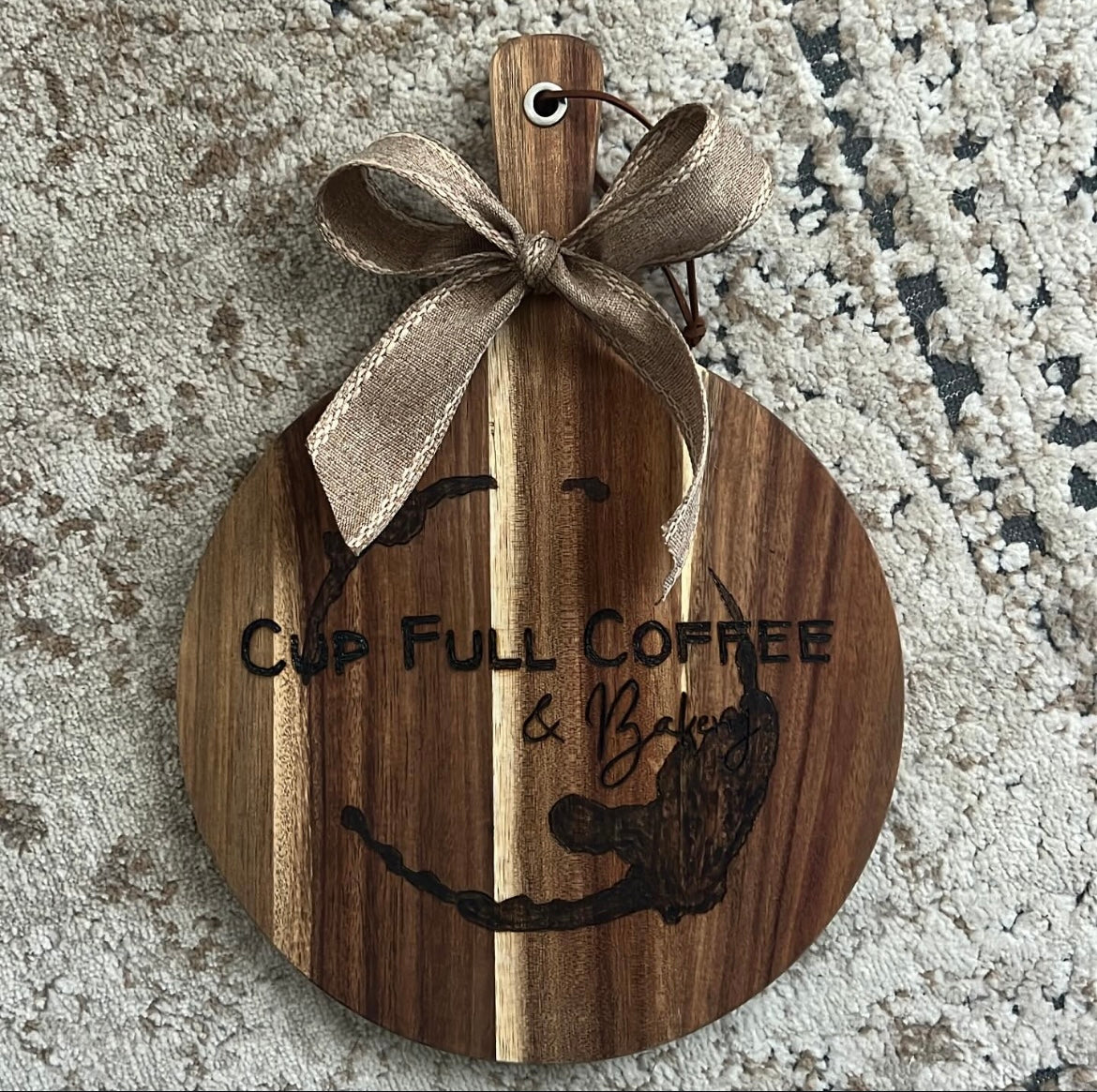 Custom wood-burned board featuring the Cup Full Coffee and Bakery logo, with detailed lettering and design on a smooth hardwood surface.