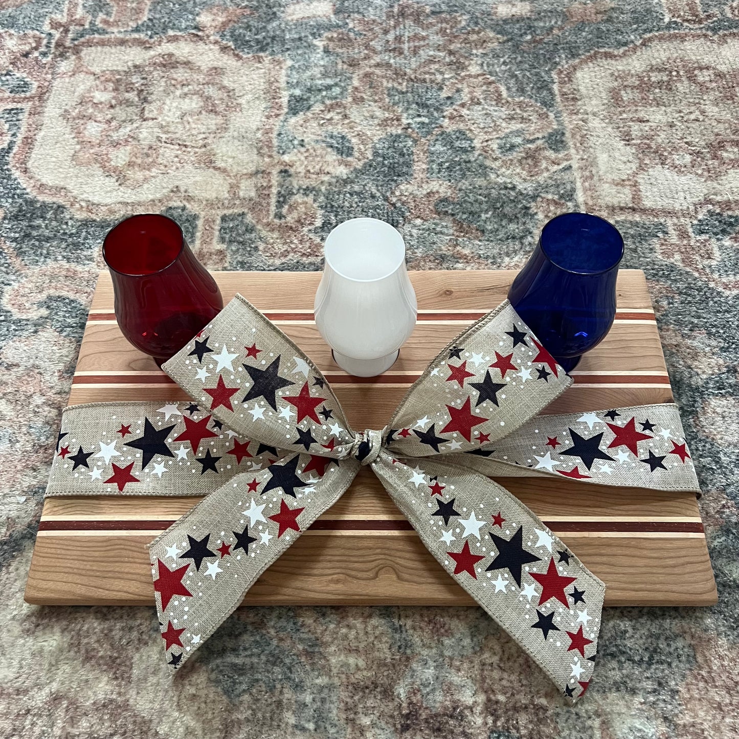 Handcrafted Fourth of July bourbon flight board made from padauk, maple, and cherry wood, featuring red, white, and blue Glencairn-style glasses 