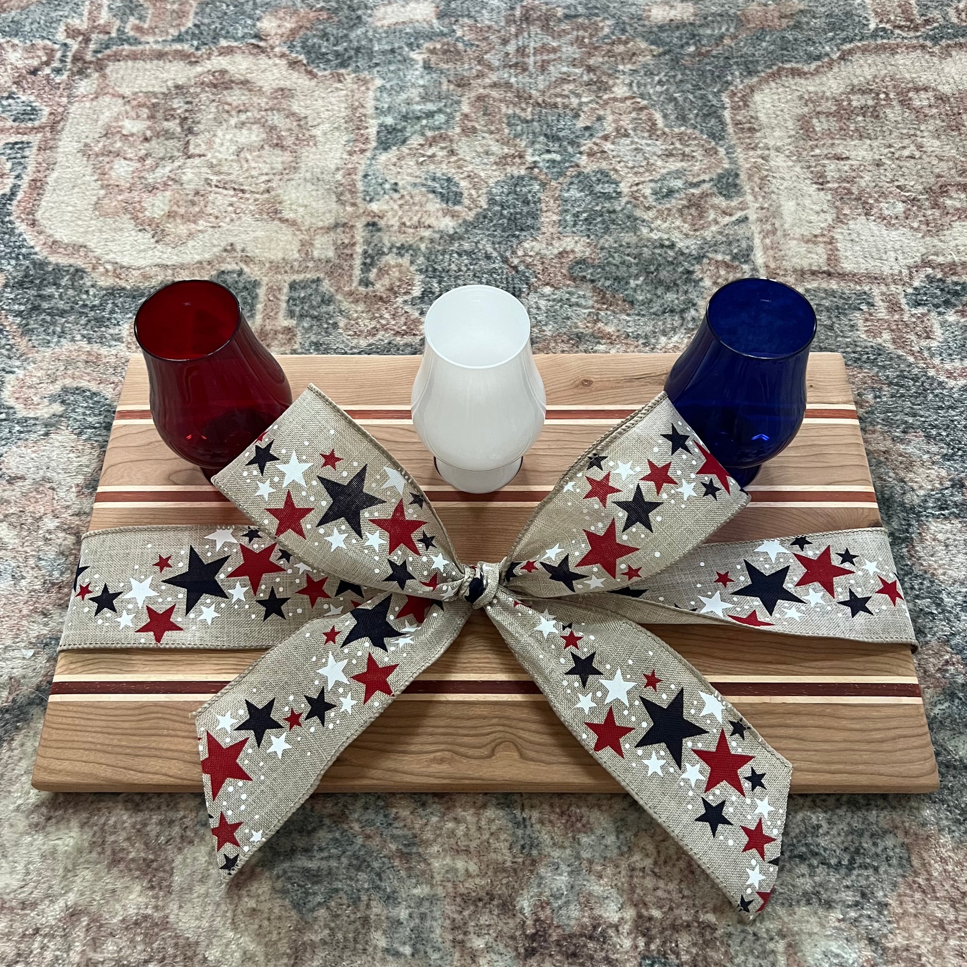 Handcrafted Fourth of July bourbon flight board made from padauk, maple, and cherry wood, featuring red, white, and blue Glencairn-style glasses 